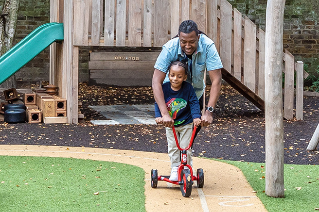 A nursery educator and child playing with a tricycle