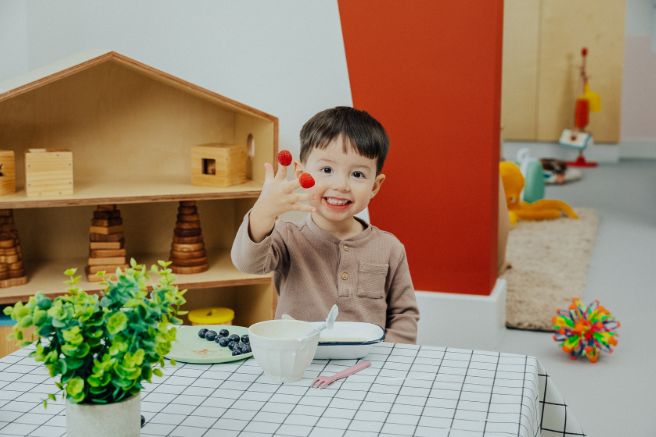 A little boy with raspberries on his fingers smiling