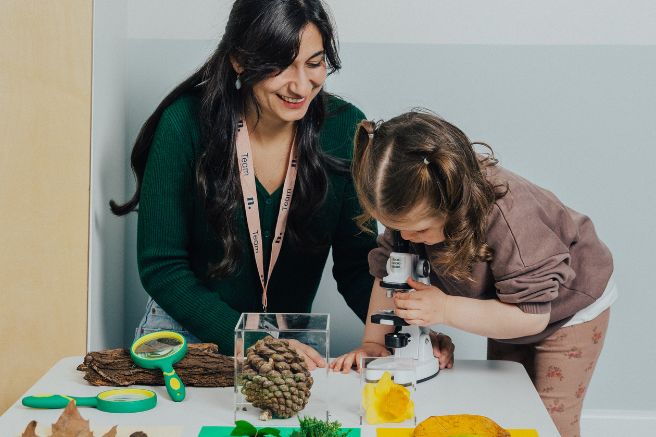 An educator sitting next to a child while the child looks through a microscope