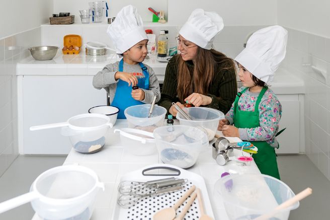 An educator and two children with chef hats on, cooking in a nursery atelier