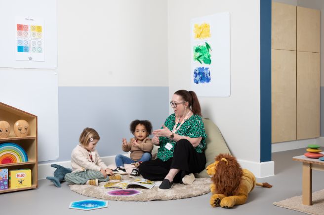 An educator and two toddlers sitting on the floor in a nursery and playing