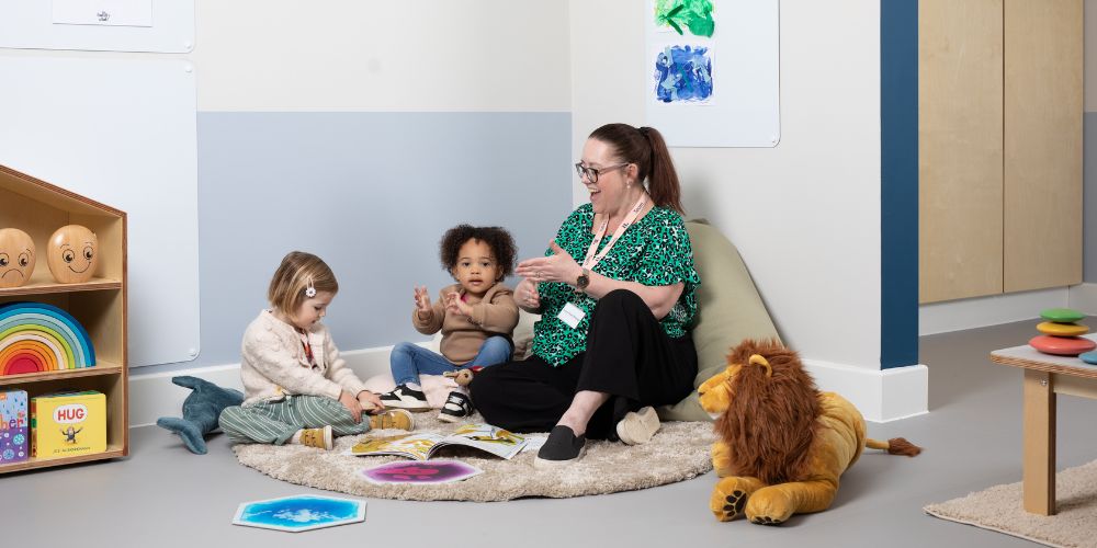 An educator and two toddlers sitting on the floor in a nursery and playing