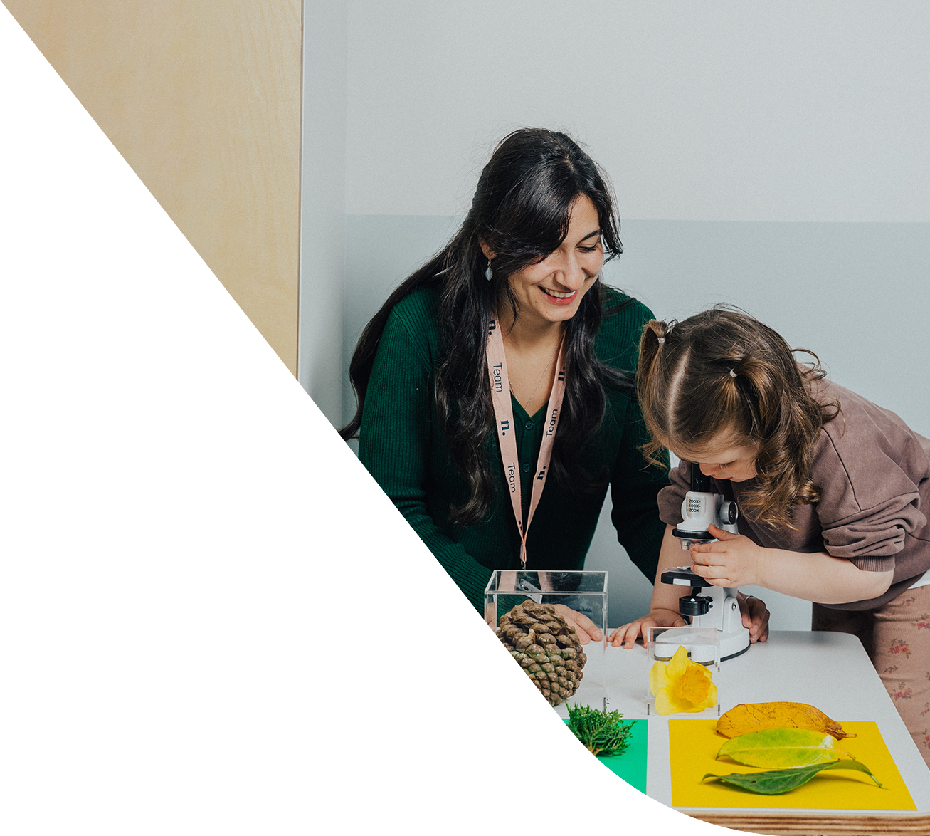 An educator sitting next to a child while the child looks through a microscope