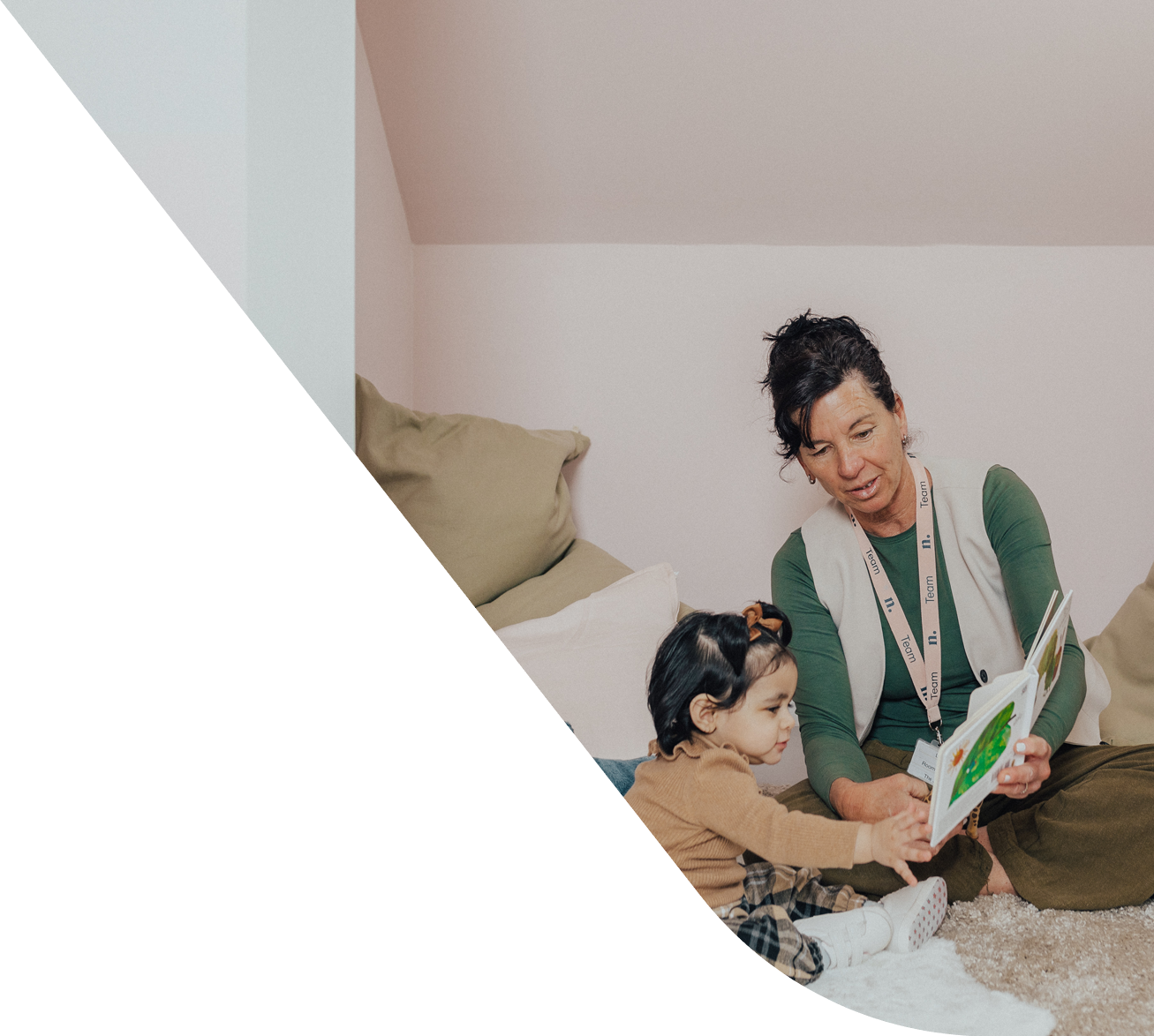 An educator reading to a toddler while sitting on the floor in a nursery playroom