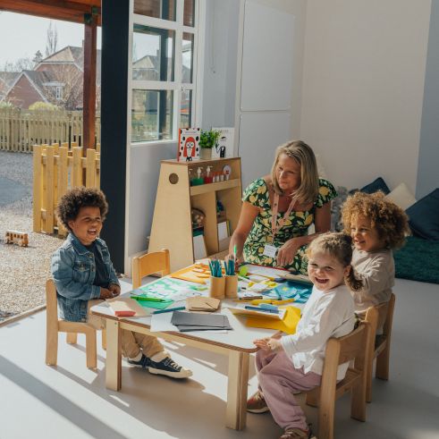 Children sitting at a desk in a nursery and drawing with their educator