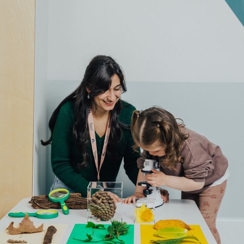 An educator sitting next to a child while the child looks through a microscope