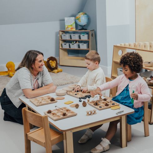 An educator smiling at two children in a nursery playroom