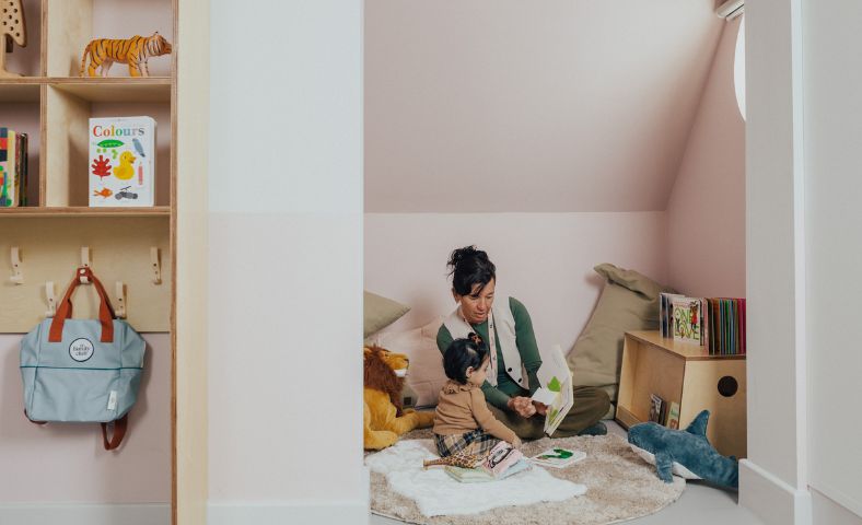 An educator reading a book to a toddler in a nursery