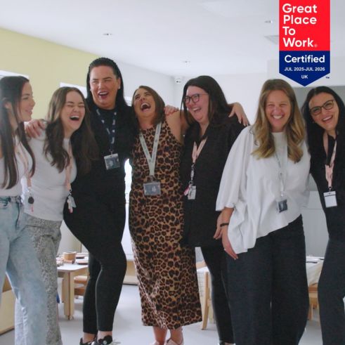 A group of smiling educators stand together, laughing. A "Great Place to Work Certified" badge is displayed in the top right corner.
