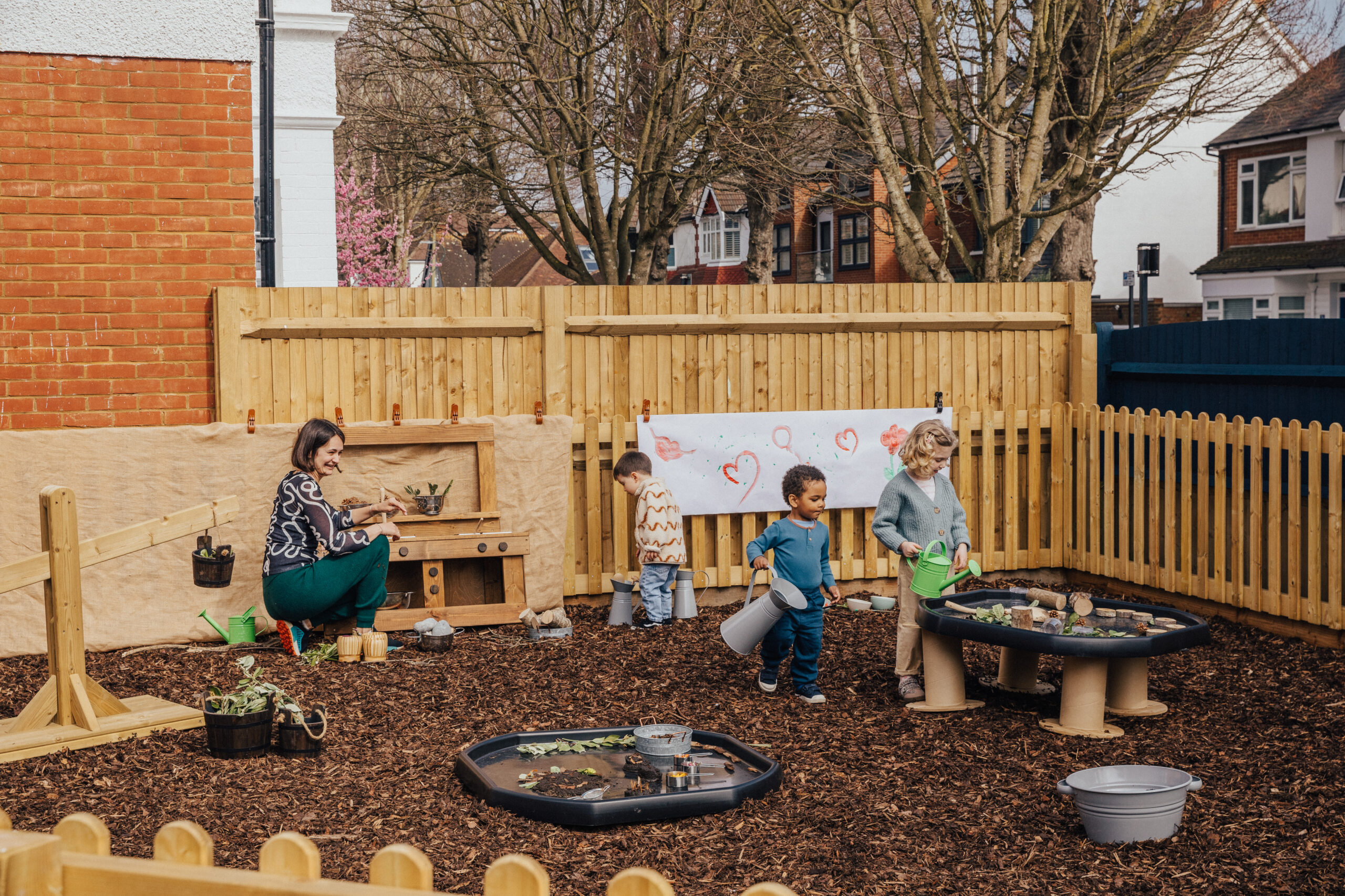 An educator and two children playing in a nursery garden